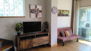A modern living room with a flat-screen TV, wooden cabinet, potted plants, a pink sofa, and a cityscape painting. - L'Instant Sud in Châteauneuf-de-Grasse (Châteauneuf-Grasse)