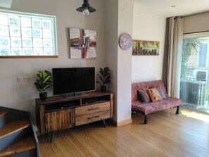 A modern living room with a flat-screen TV, wooden cabinet, potted plants, a pink sofa, and a cityscape painting. - L'Instant Sud in Châteauneuf-de-Grasse (Châteauneuf-Grasse)