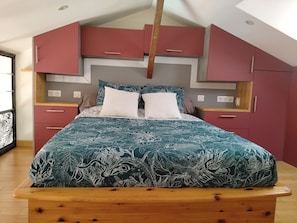 A bedroom with a bed, a wooden headboard, a red wardrobe, and a window. - L'Instant Sud in Châteauneuf-de-Grasse (Châteauneuf-Grasse)