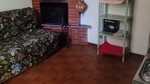 A living room with a fireplace, a sofa, a green shelf with kitchen items, and a tiled floor.