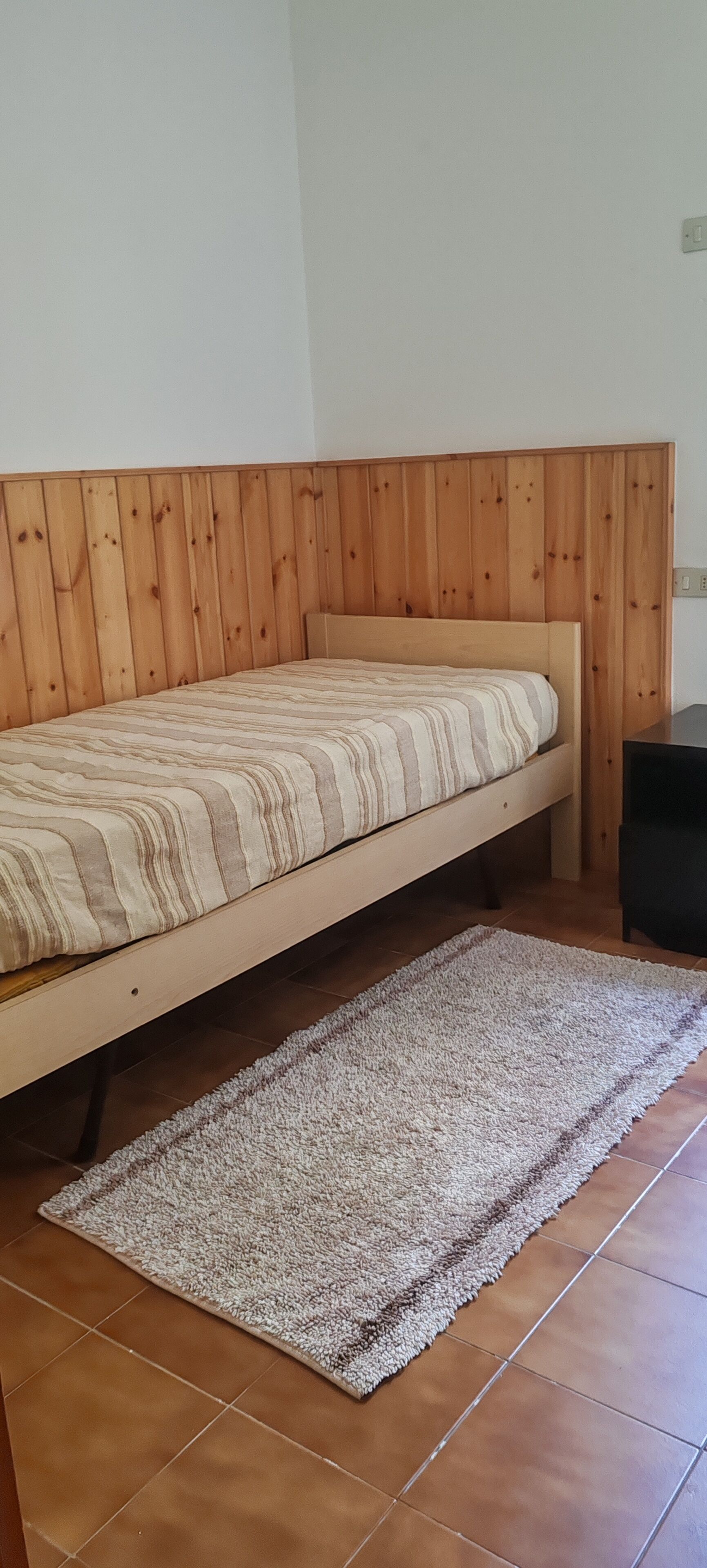 Een eenpersoonsbed met houten hoofdeinde in een kamer met betegelde vloer.