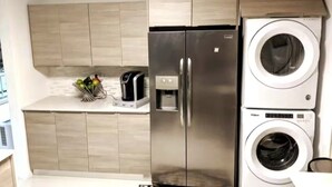 Eine kompakte Küche mit Edelstahl-Kühlschrank, integriertem Waschmaschinenanschluss und einer Kaffeemaschine auf der Arbeitsplatte.