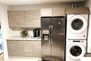 Eine kompakte Küche mit Edelstahl-Kühlschrank, integriertem Waschmaschinenanschluss und einer Kaffeemaschine auf der Arbeitsplatte.