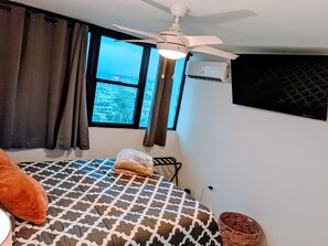 Hotelkamer met een bed, een plafondventilator, een raam met uitzicht en een wandairconditioner.