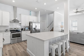 Una cocina moderna con armarios blancos, electrodomésticos de acero inoxidable y una isla central con taburetes de bar.