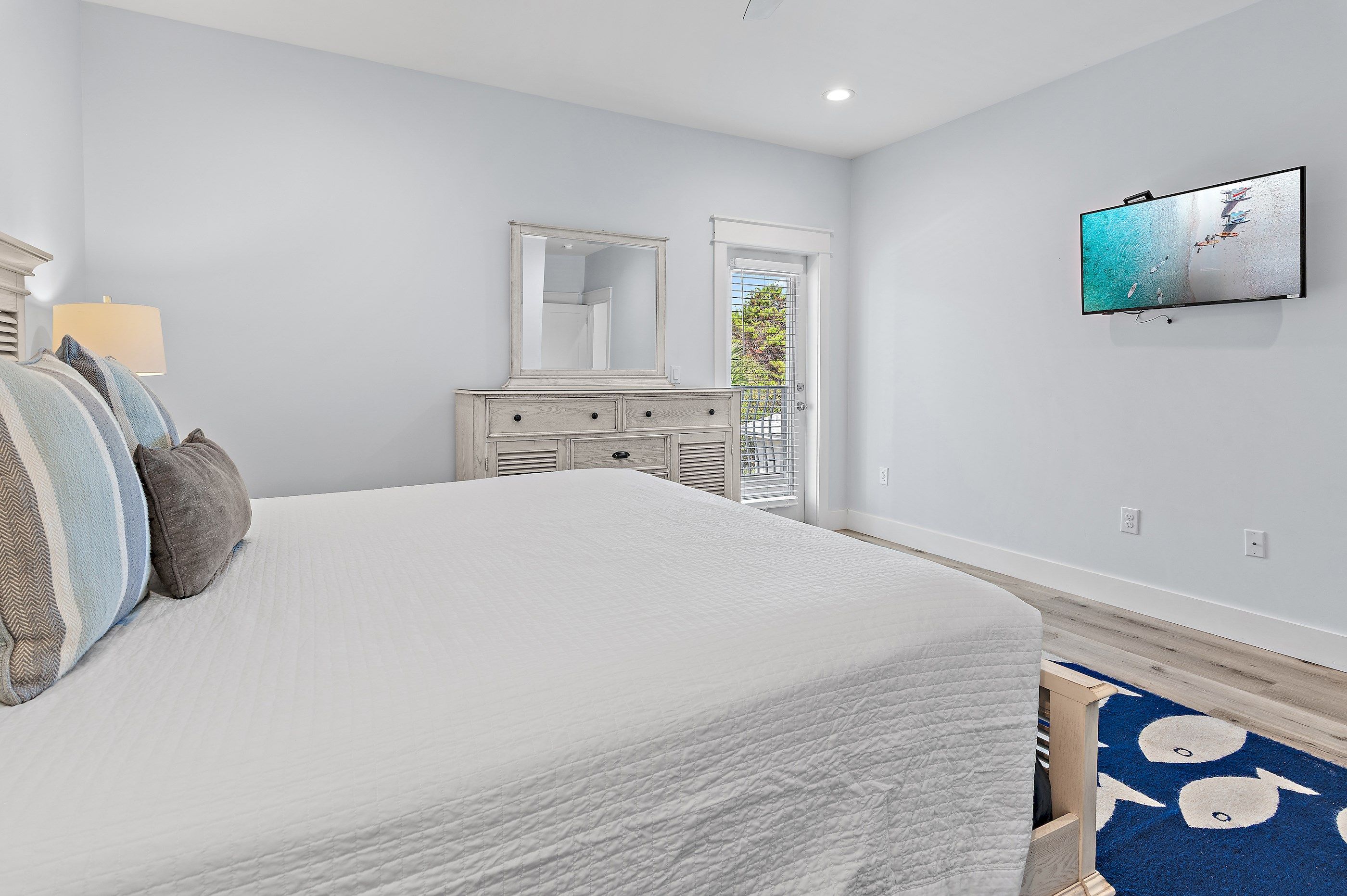 A bedroom with a large bed, a dresser, a mirror, and a television on the wall.