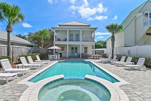 Una casa de dos pisos con piscina, mobiliario exterior y patio cercado.