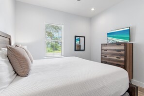 A bedroom with a large bed, a dresser, a framed picture, and a window with blinds. - Saltwater Sanctuary | Billiards, Spa, & Golf Cart (Miramar Beach)