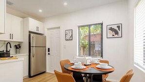 A modern kitchen with white cabinets, a stainless steel refrigerator, and a dining area with orange chairs and a round table. - 3bed Near Beach, Wynwood Design District, Brickell (Miami)