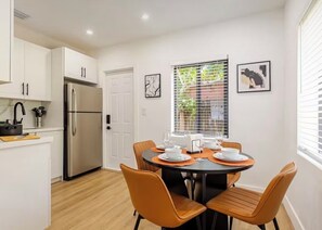 Eine moderne Küche mit weißen Schränken, einem Edelstahlkühlschrank und einem Essbereich mit orangefarbenen Stühlen und einem runden Tisch.
