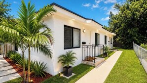 A modern two-story house with a well-maintained lawn, a paved walkway, and a small garden area with palm trees. - 3bed Near Beach, Wynwood Design District, Brickell (Miami)