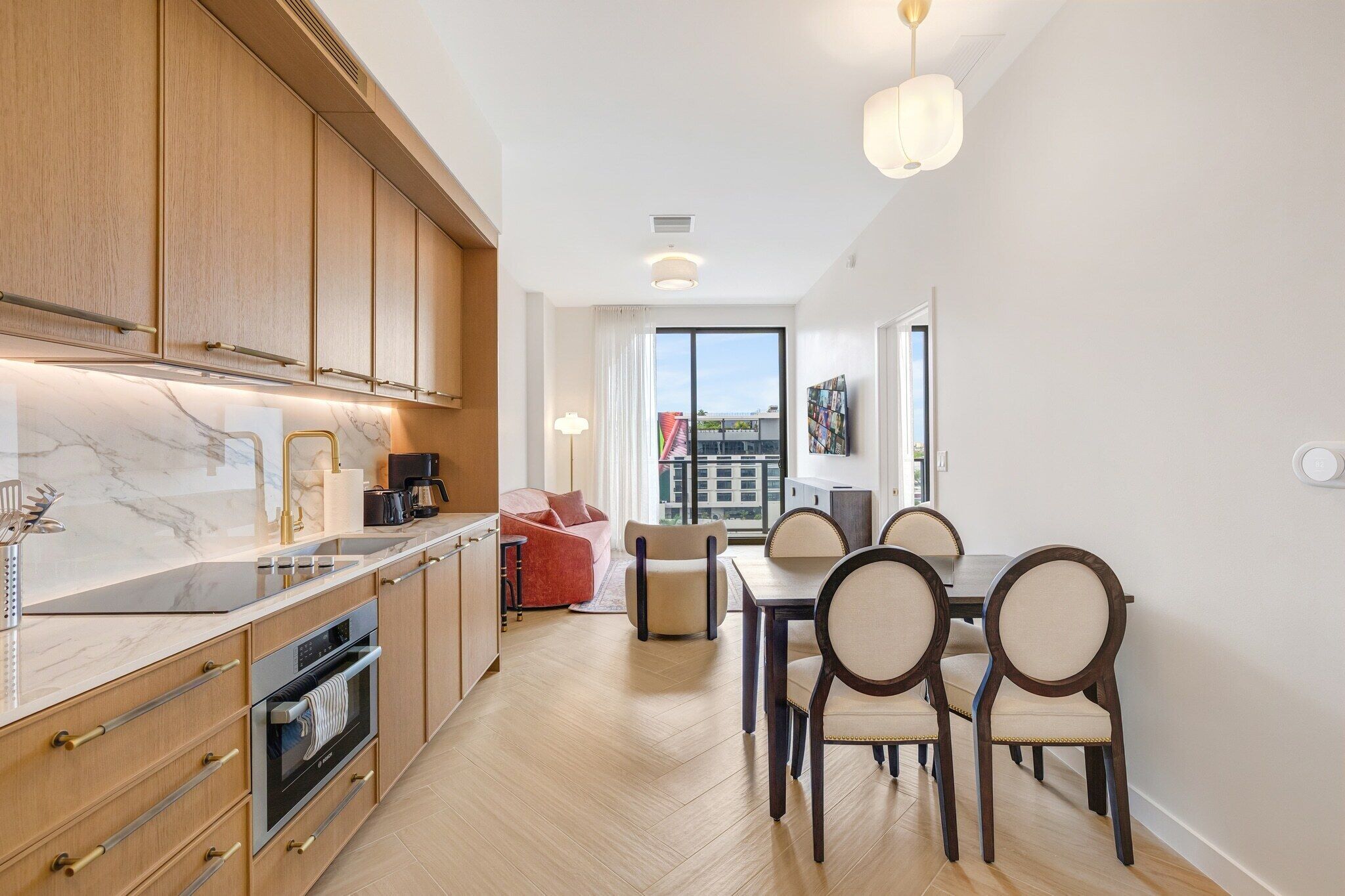 A modern kitchen with wooden cabinets, a marble countertop, and a dining area with a table and chairs.