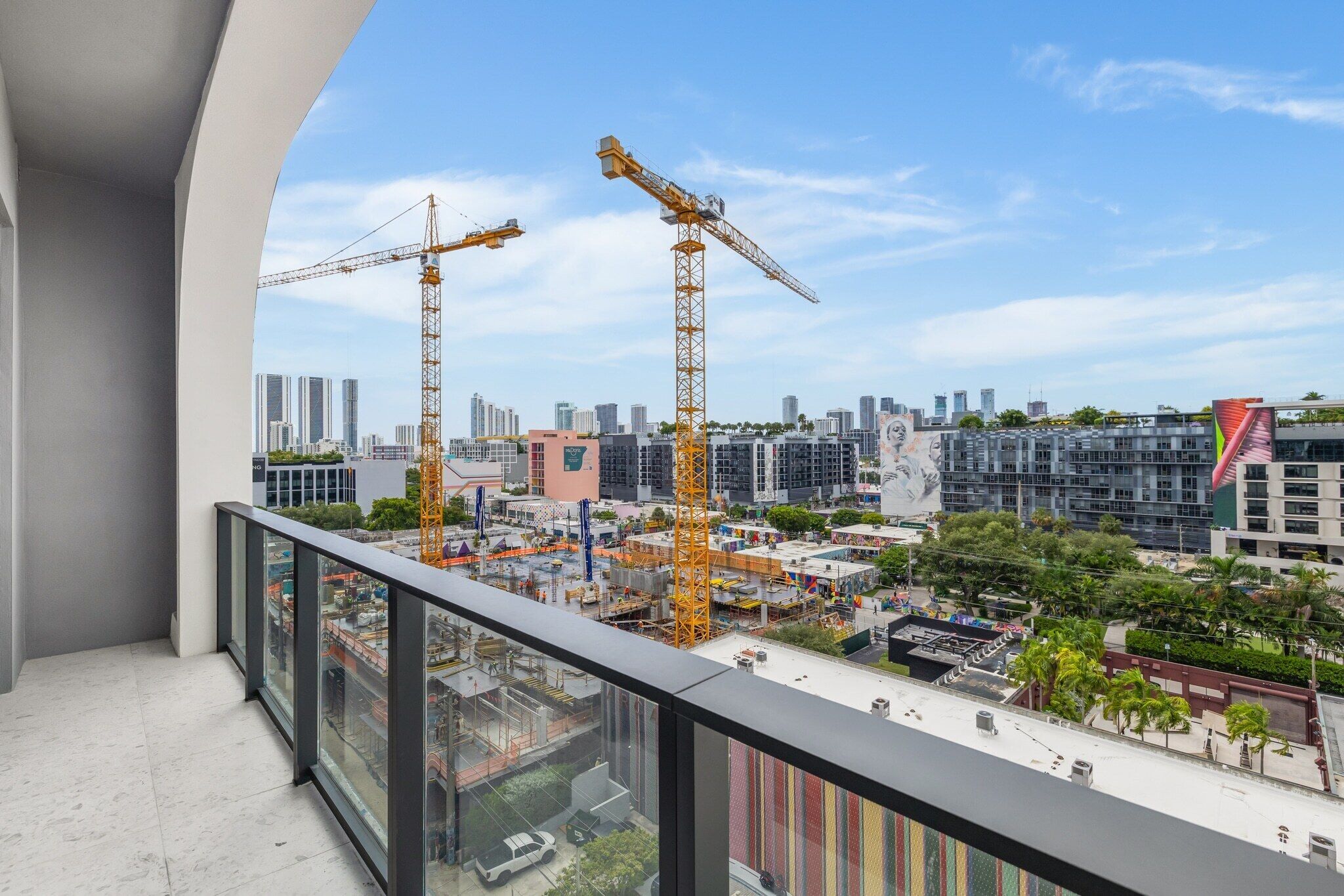 Een balkon met uitzicht op een bouwplaats, met twee kraanarmen en een stadsbeeld met moderne gebouwen.