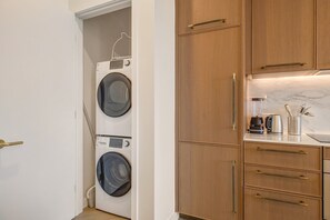 Un lavadero con dos lavadoras de carga frontal, armarios de madera y una zona de cocina con licuadora y utensilios.