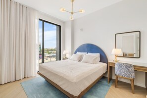 A hotel room with a large bed, a desk with a chair, a mirror, and a view of the city through the window. - Chic Miami Apt Pool Gym & Sleeps 4 (Miami)