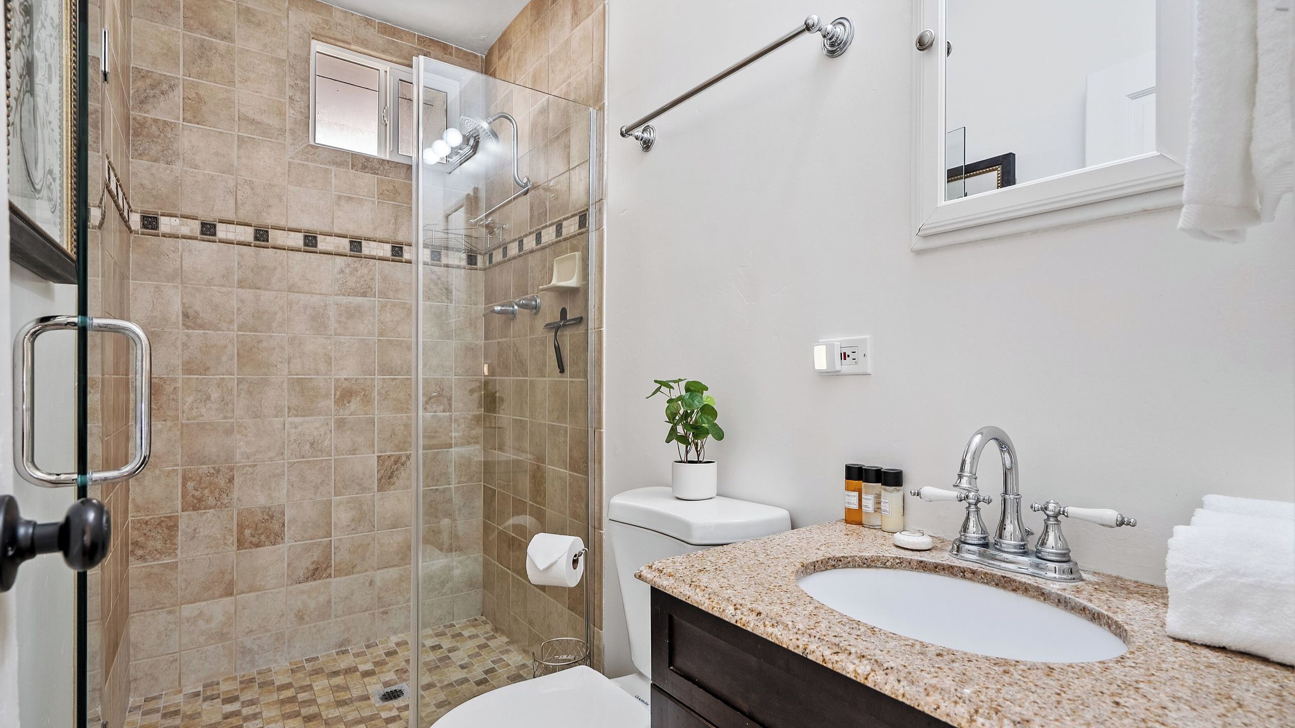 Un baño con cabina de ducha de vidrio, lavamanos con encimera de mármol y un inodoro.