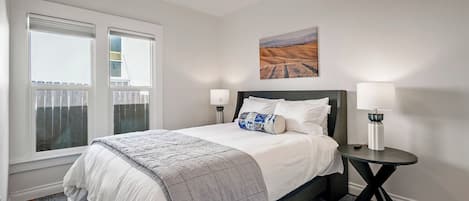 A bedroom with a bed, two bedside lamps, a window, and a painting on the wall.