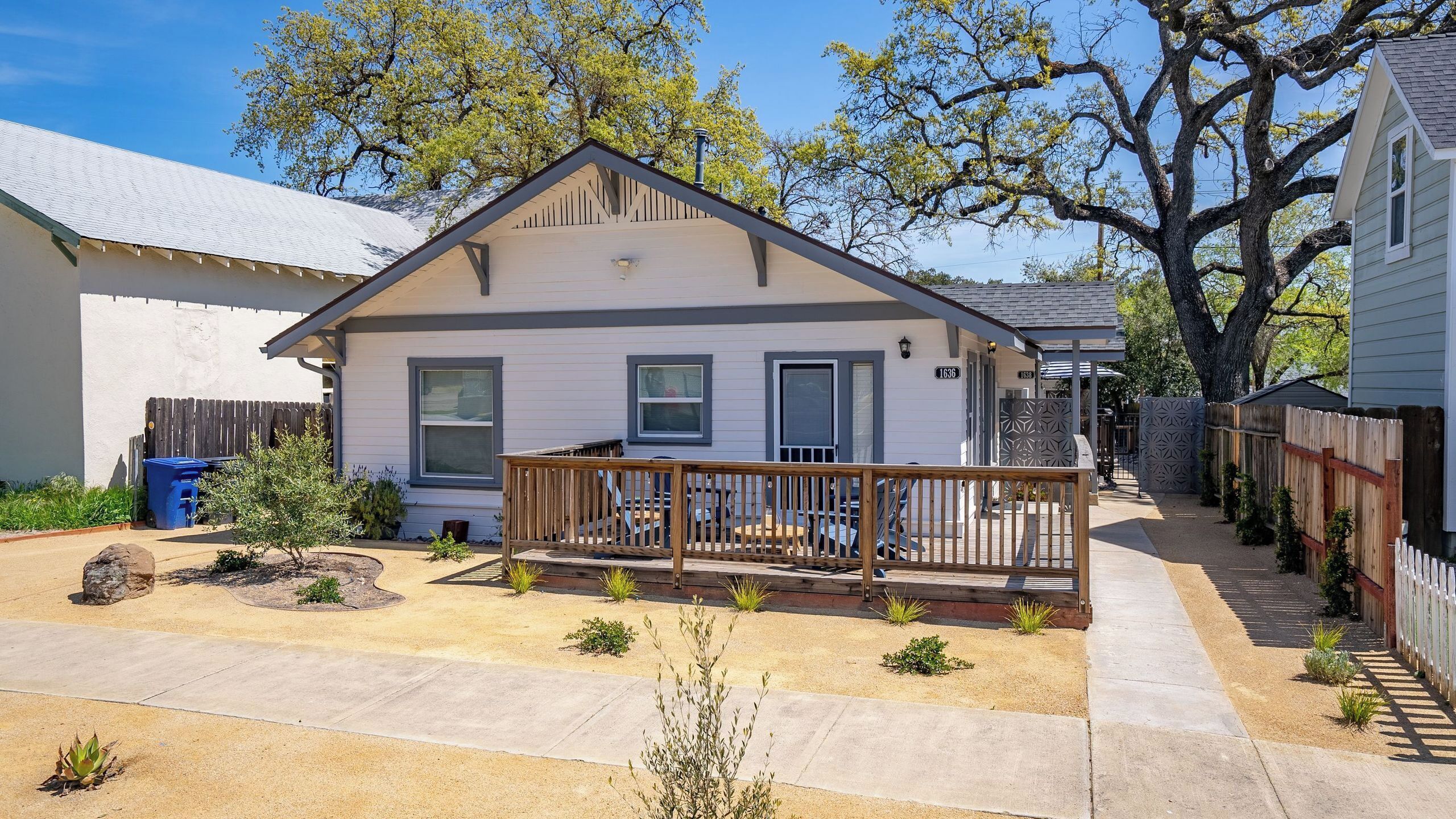 A single-story house with a front porch, a small yard, and a tree in the background.