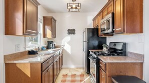 A kitchen with wooden cabinets, a stainless steel refrigerator, a stove, and a microwave. - Paso on Oak by Avantstay Cottage-style Home + Full Kitchen + Front Deck Near Downtown (Paso Robles)