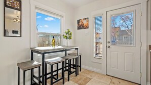 A kitchen with a bar area, a white door, and a window with blinds. - Paso on Oak by Avantstay Cottage-style Home + Full Kitchen + Front Deck Near Downtown (Paso Robles)