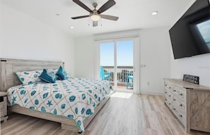 Ein Schlafzimmer mit einem Bett, Deckenventilator, Fernseher, Kommode und einem Balkon mit Blick.
