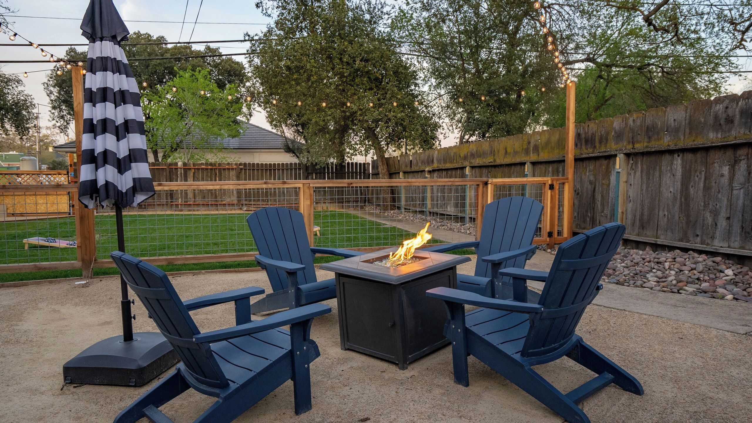 Un patio con cuatro sillas Adirondack, una mesa cuadrada y un pozo de fuego.