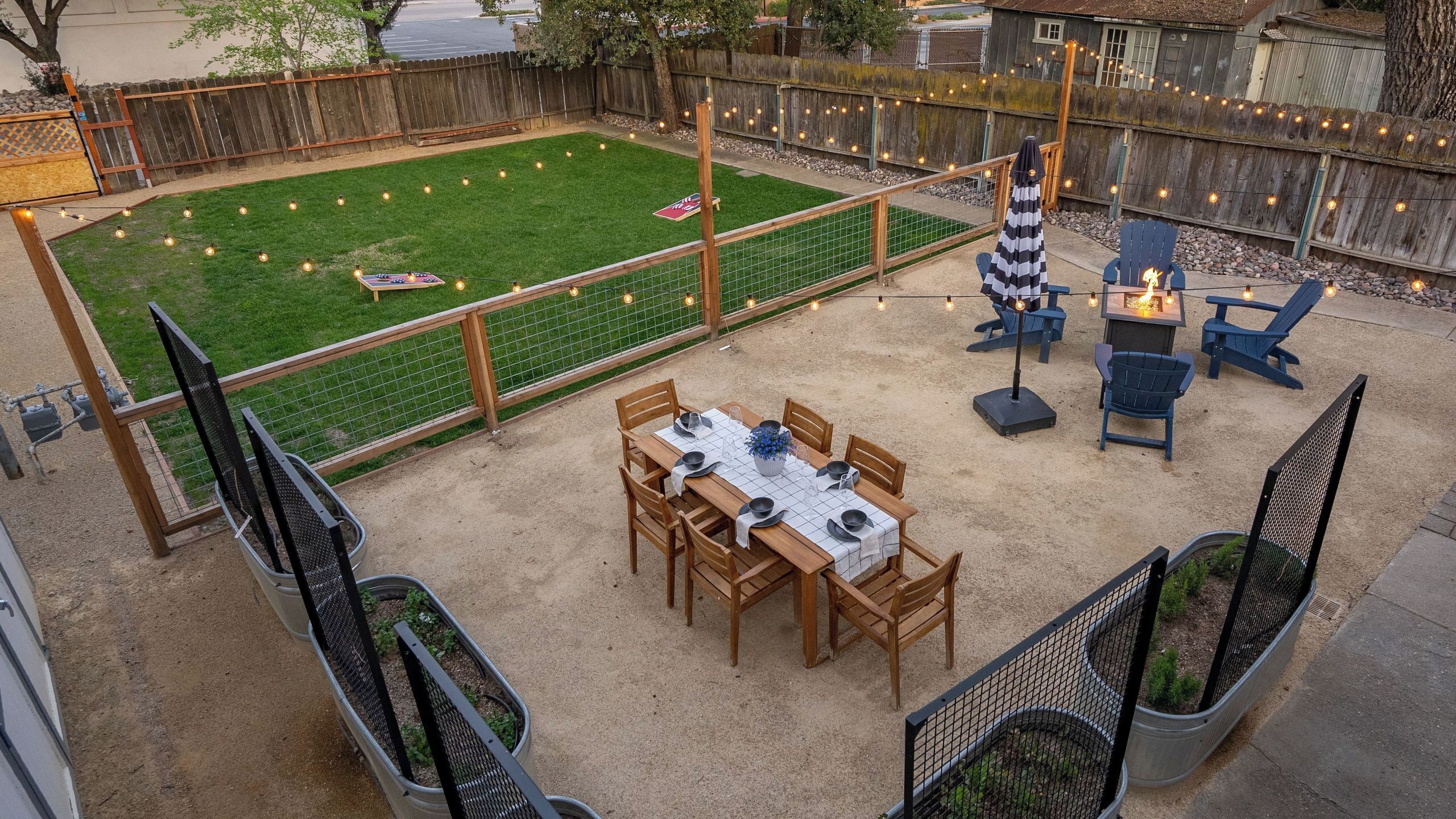 An outdoor patio with a table set for dining, surrounded by chairs, and a fire pit area with chairs.