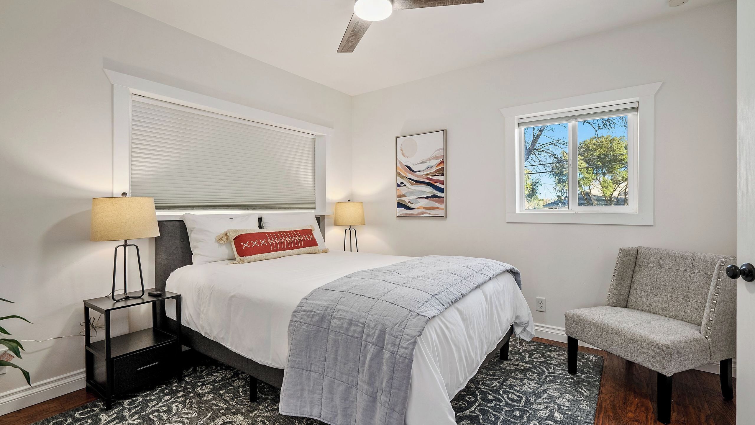 A bedroom with a bed, two bedside lamps, a chair, a window, and a ceiling fan.