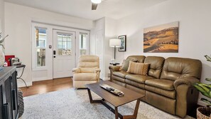 Ein Wohnzimmer mit einem beigefarbenen Sessel, einem braunen Ledersofa, einem Couchtisch und einem gerahmten Landschaftsbild an der Wand.