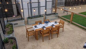 Un área de comedor al aire libre con una mesa preparada para cuatro personas, rodeada de sillas y una guirnalda de luces arriba.