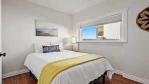 Un dormitorio con cama, ventana, lámpara de pared y un cuadro.