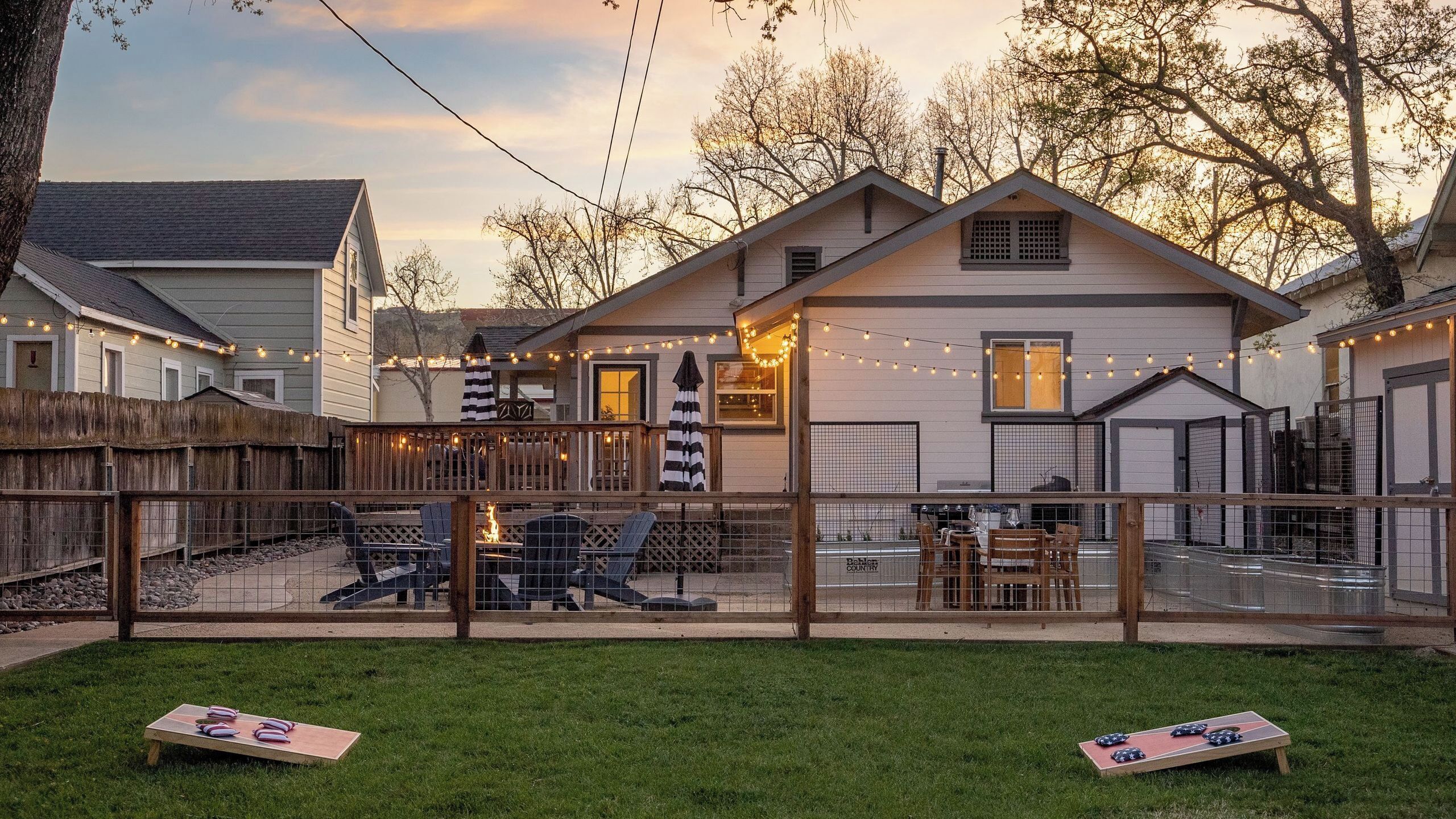 A backyard with a wooden deck, outdoor seating, and string lights.