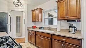 Una cocina con armarios de madera, un refrigerador de acero inoxidable, una estufa a gas, una cafetera y una ventana sobre el fregadero.