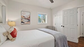 A bedroom with a bed, a window, a door, and a wall-mounted lamp.