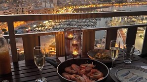 Ett bord dukat för två personer med skaldjur, ett ljus och glas på en balkong med utsikt över stadsbilden.