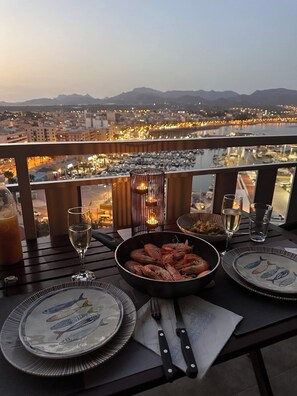 Ein Tisch für zwei Personen mit Meeresfrüchten, einer Kerze und Gläsern auf einem Balkon mit Blick auf eine Stadtlandschaft.