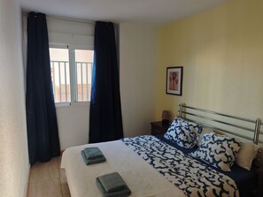 Ein Hotelzimmer mit einem Bett, einem Nachttisch, einer Lampe, einem gerahmten Bild an der Wand und einem Fenster mit Vorhängen.