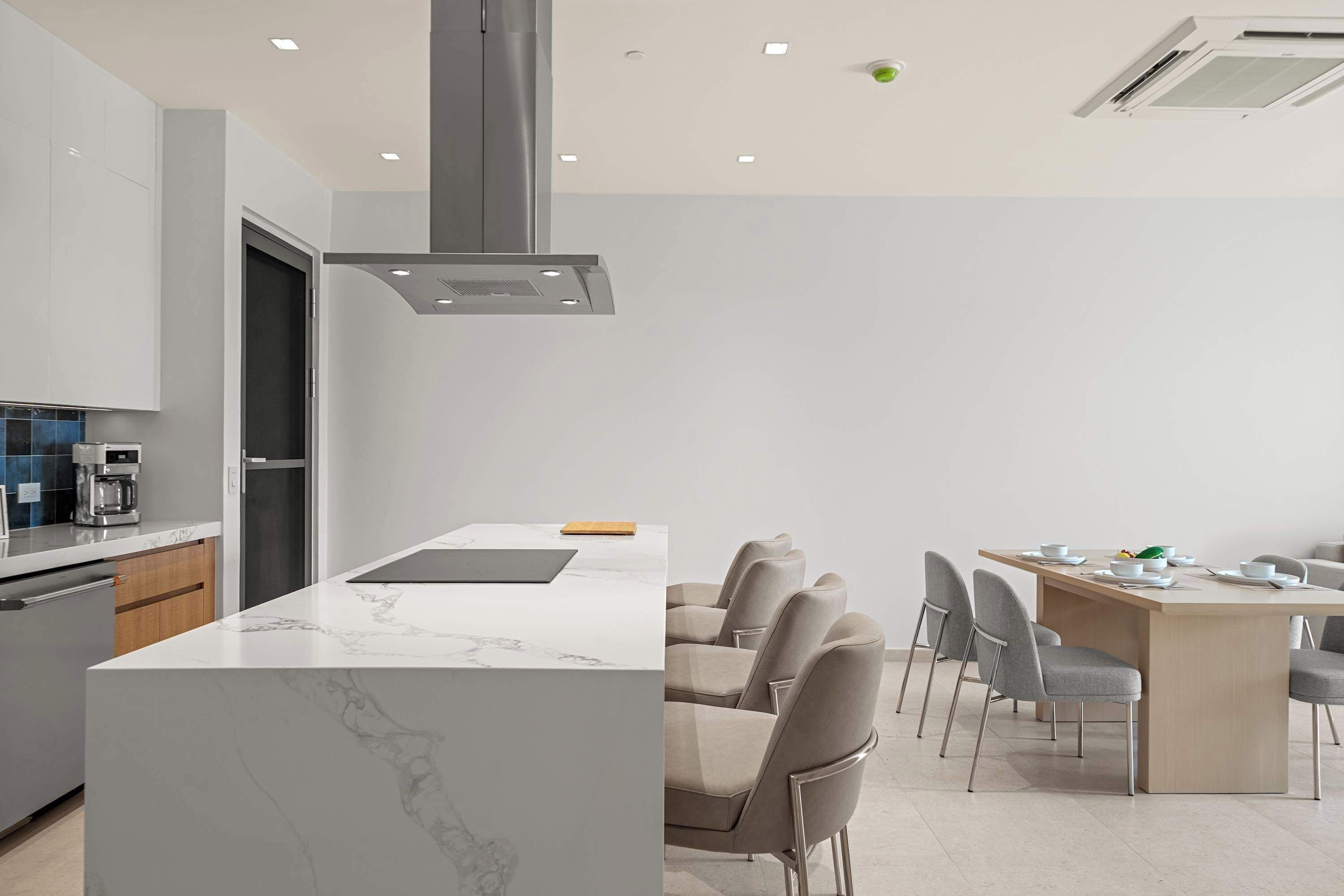 Una cocina moderna con una isla central, electrodom ésticos integrados y un comedor con sillas y mesa.
