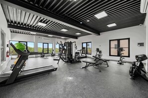 A gym with exercise equipment, large windows, and a high ceiling. - Sunset Balcony | 3BR | 5-Min Drive to Eagle Beach (Noord)