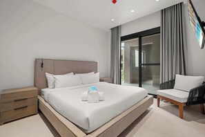 Una habitación de hotel moderna con una cama grande, una mesita de noche, una silla y vistas a través de un ventanal.