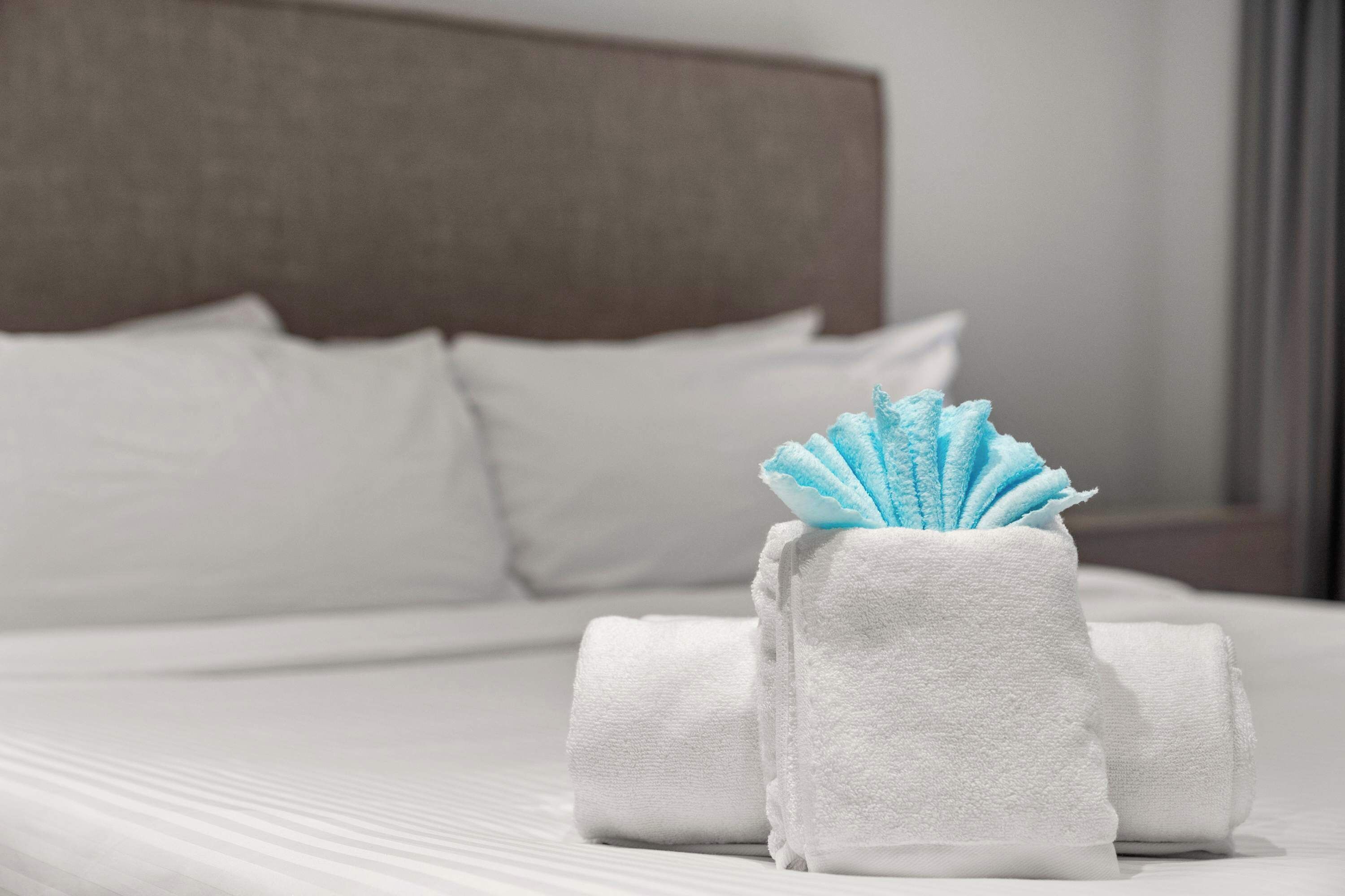Cama bien hecha con sábanas blancas y una toalla doblada de color azul.