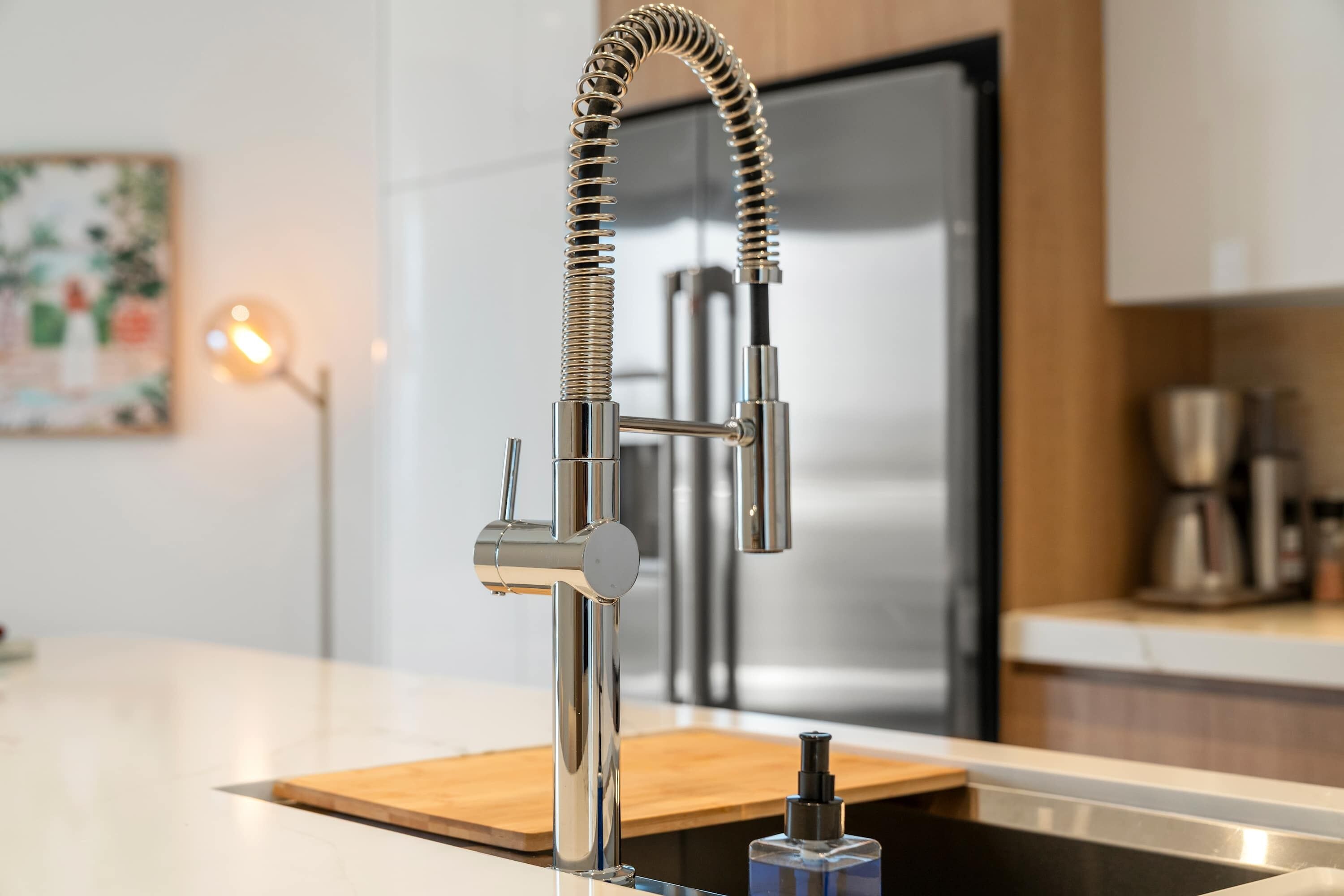 A modern kitchen with a stainless steel faucet, a wooden countertop, and a stainless steel refrigerator in the background.