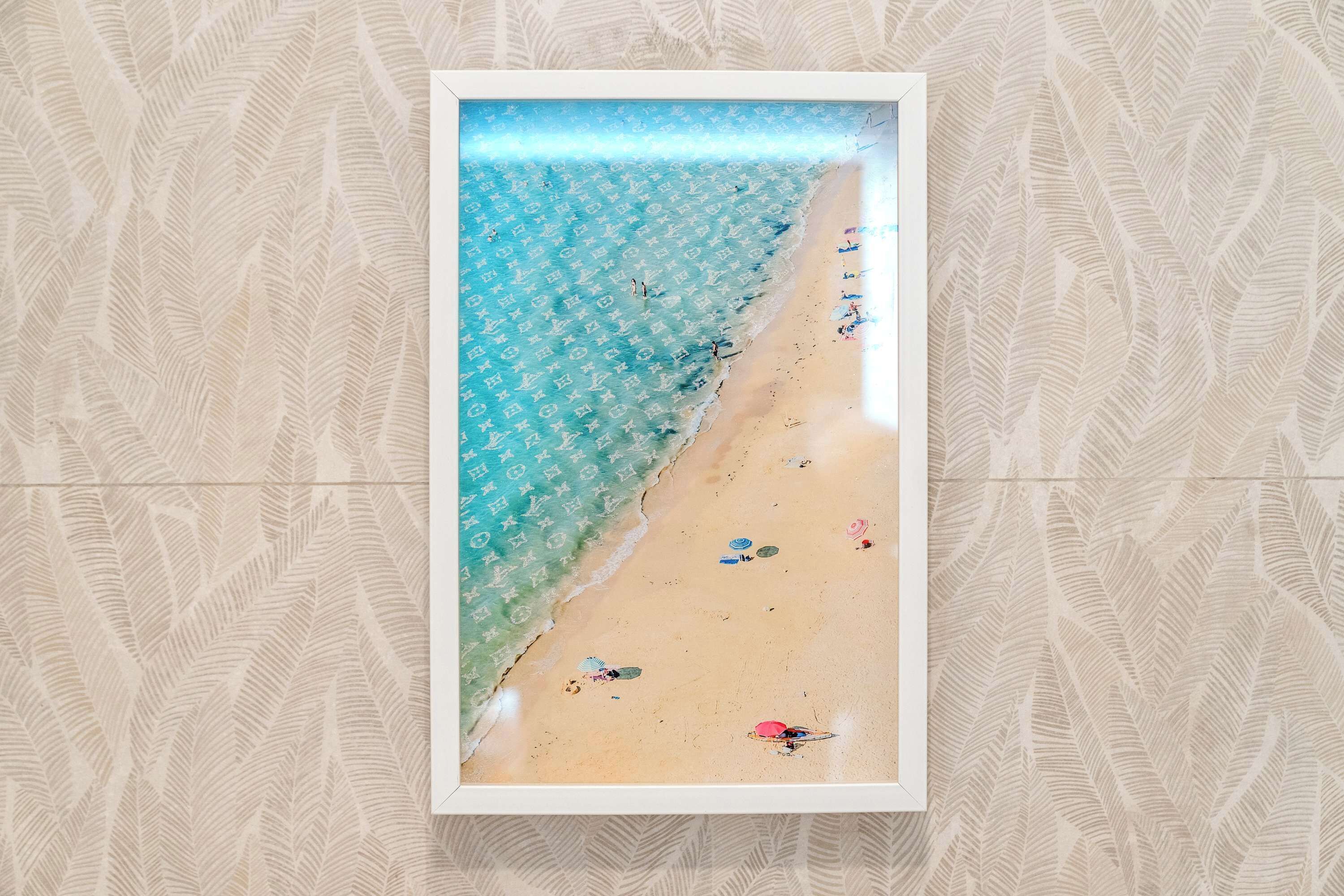 A framed beach scene with a clear sky, calm sea, and a sandy shore with umbrellas and beachgoers.