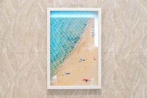 Une image encadrée représentant une scène de plage, avec un ciel dégagé, une mer calme et une plage de sable où l’on voit des parasols et des personnes se prélassant au soleil.