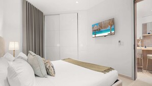 Una camera da letto moderna con un letto grande, una televisione montata a parete e un bagno visibile attraverso una porta aperta.