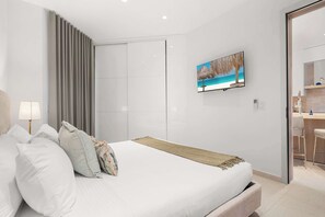 Ein modernes Schlafzimmer mit einem großen Bett, einem an der Wand befestigten Fernseher und einem durchgegangenen Tür erkennbaren Badezimmer.