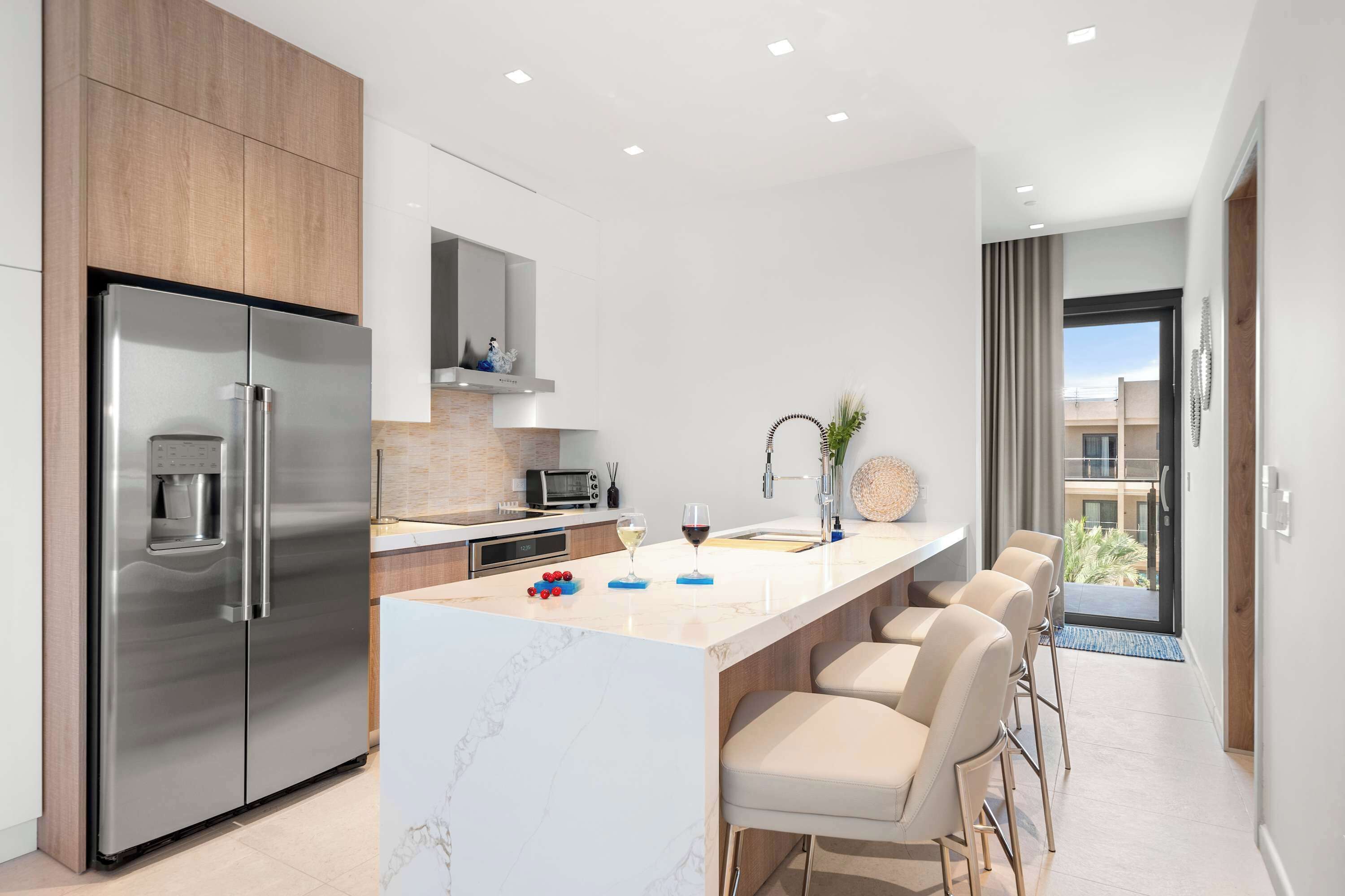 A modern kitchen with a large island, stainless steel appliances, and a view to the outside.