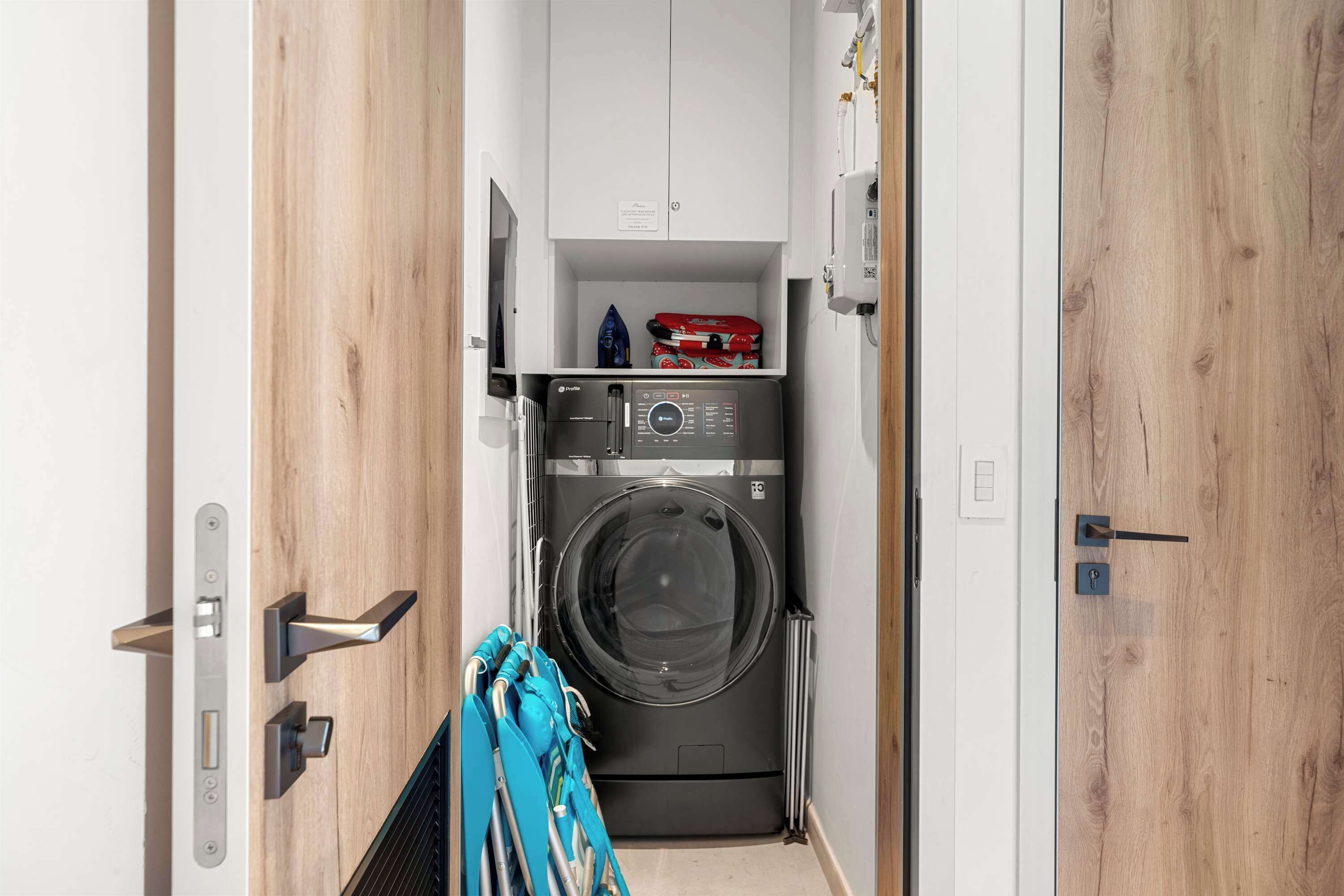 A compact laundry room with a front-loading washing machine, a drying rack, and a small shelf with items.