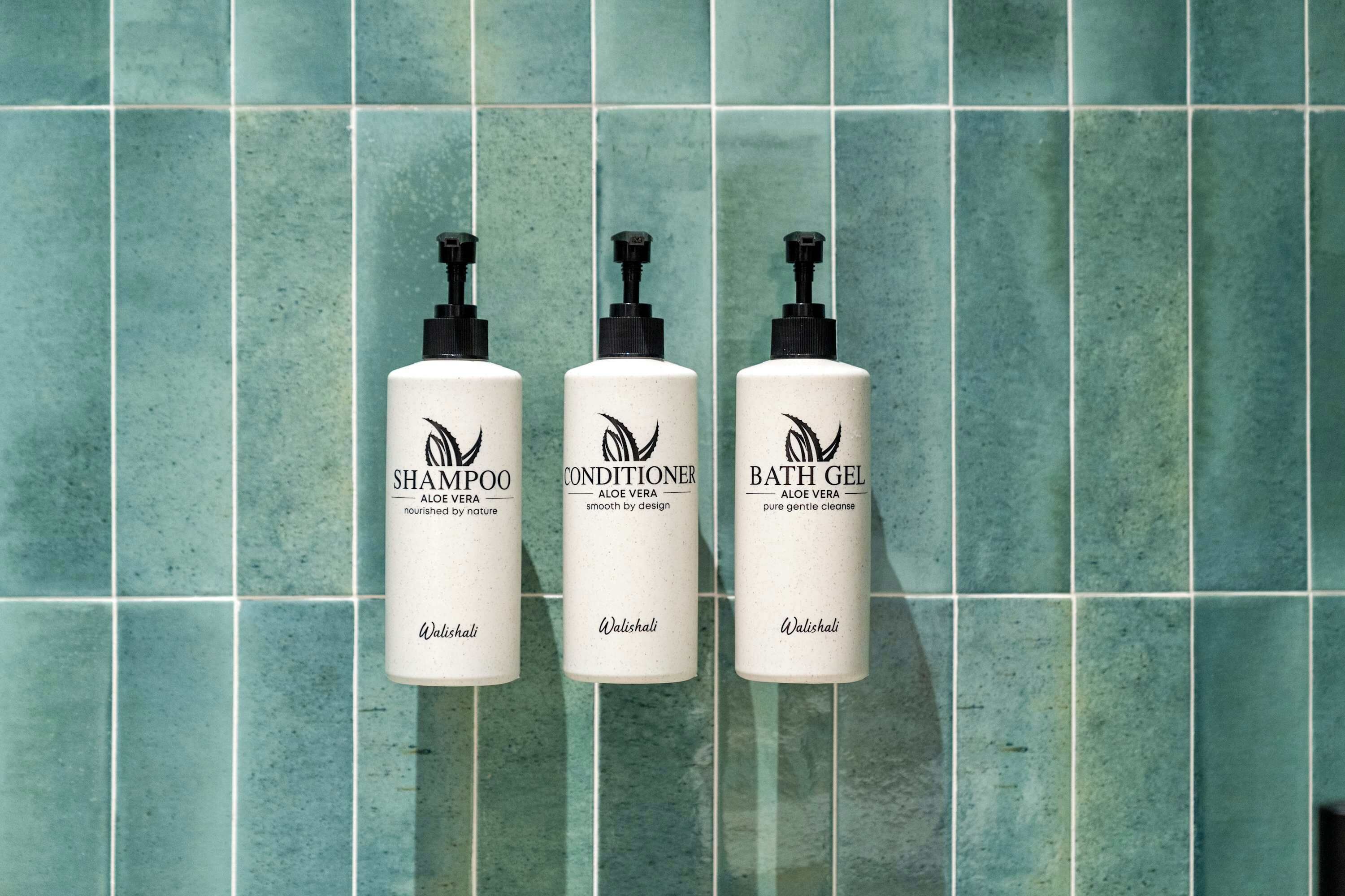 Tres botellas de champú, acondicionador y gel de baño sobre una pared de azulejos.