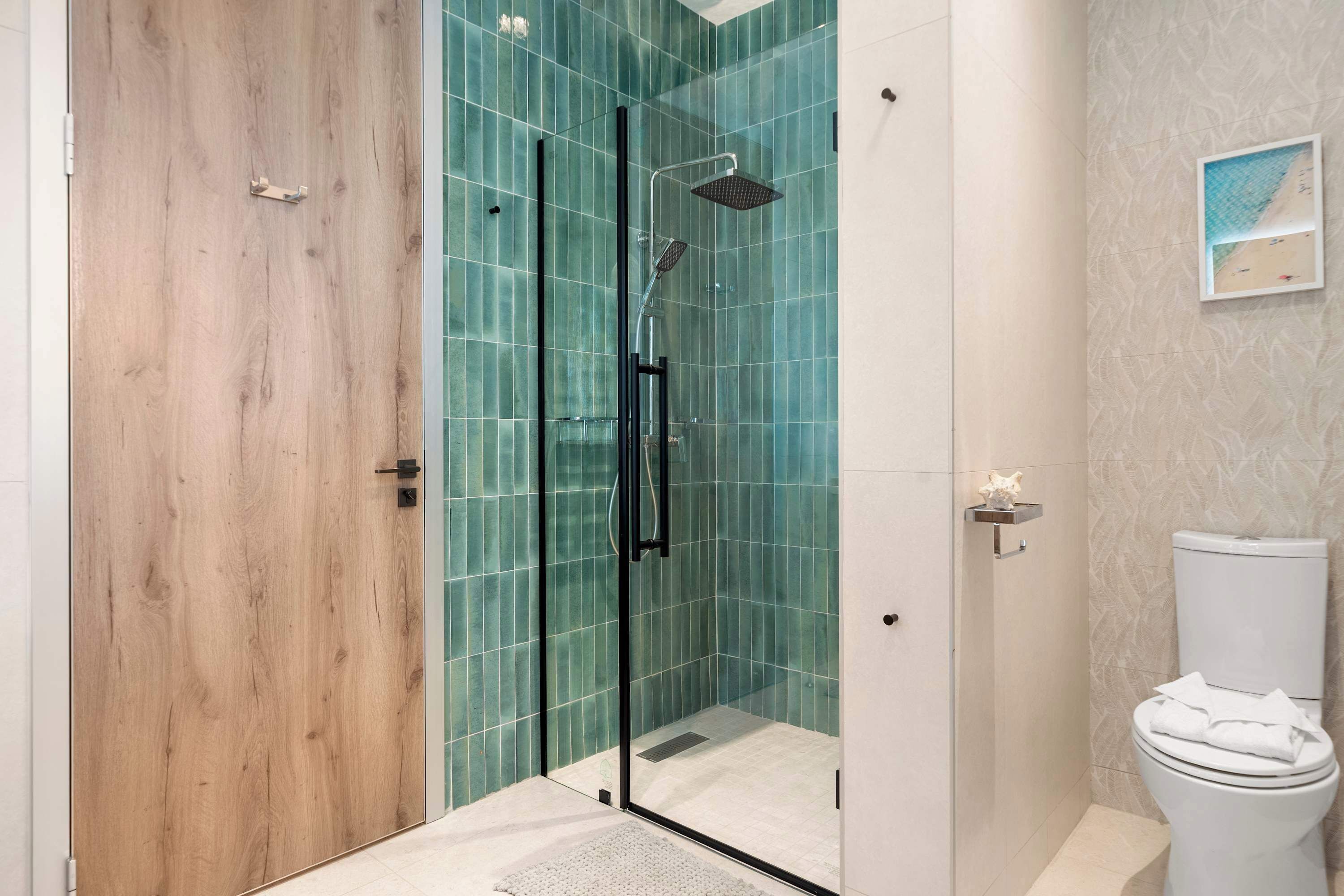 A modern bathroom with a glass-enclosed shower, a wooden door, and a toilet with a towel on top.